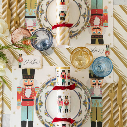 An elegant table setting with the Gold Peppermint Stripe Runner under the Nutcracker Placemat, Gold Peppermint Stripe Guest Napkin and Nutcracker Place Card with the name &quot;Debbie&quot; written in cursive.