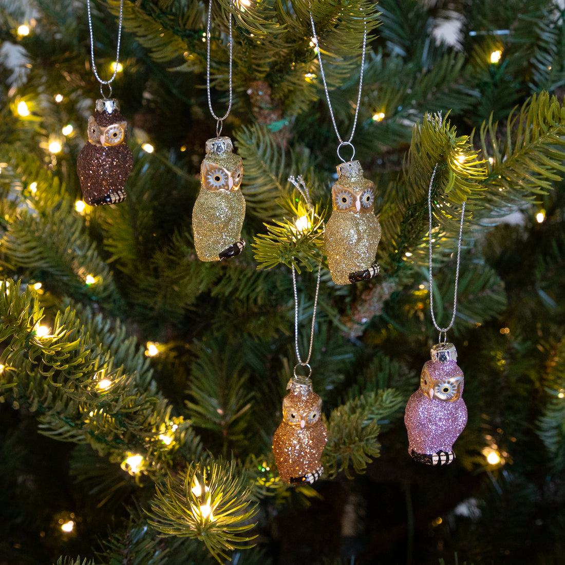 Decorative owl ornaments on a Christmas tree with lights.