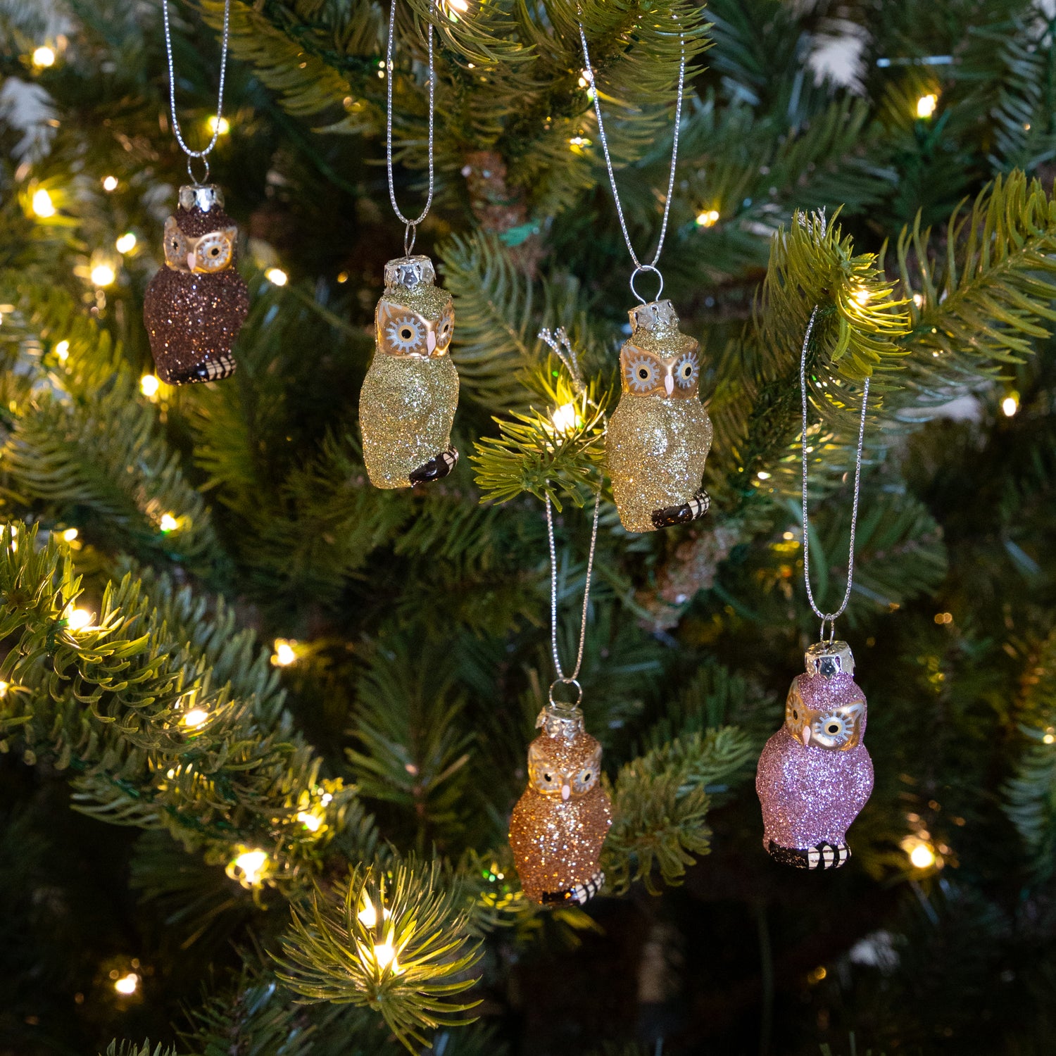 Decorative owl ornaments on a Christmas tree with lights.
