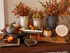 A table featuring various pottery pieces with a Fall theme and dried leaves. 