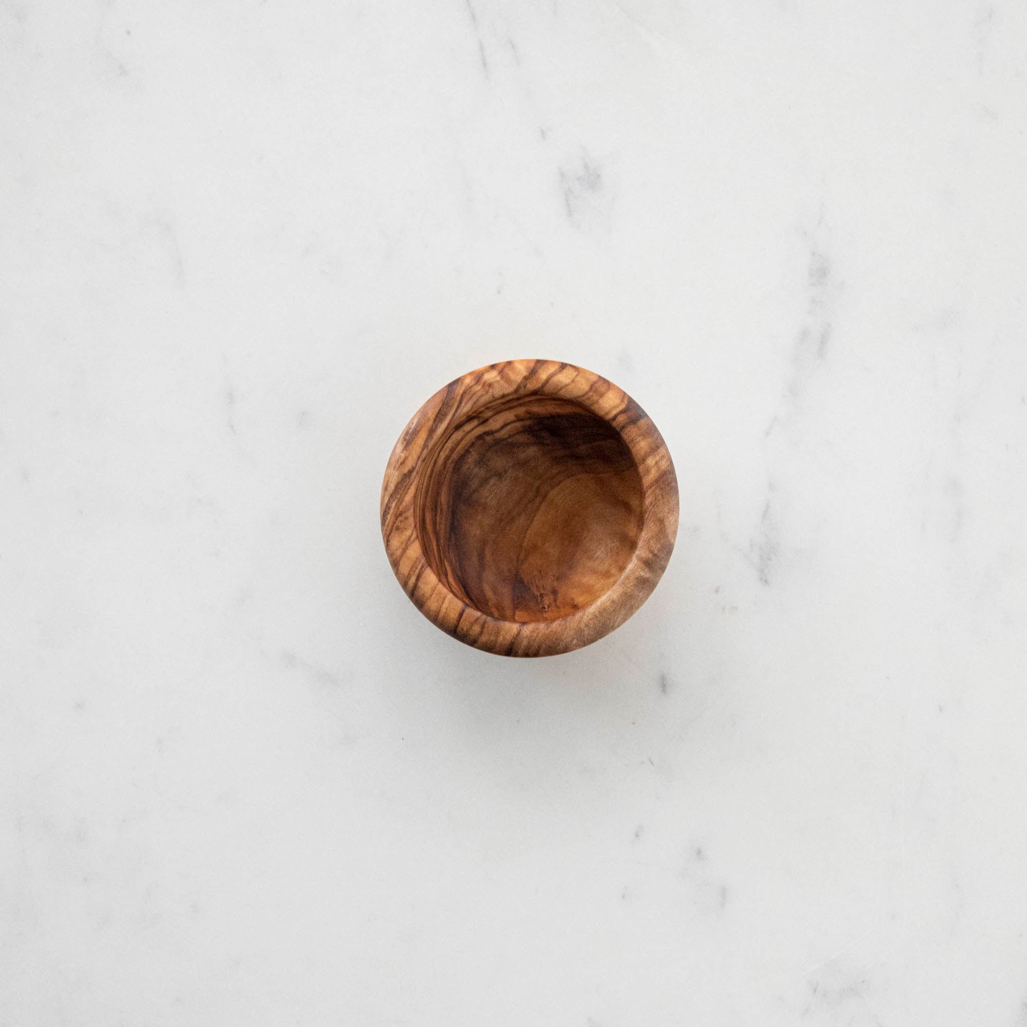 Three Natural Olivewood Pinch Bowls with salt and a sprig of rosemary on a kitchen counter.