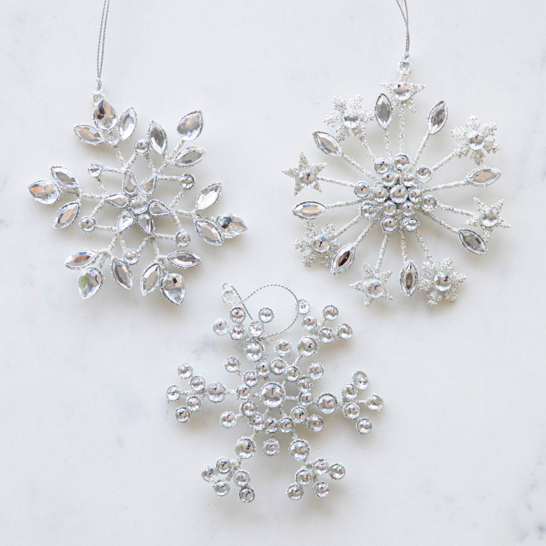 Three assorted Crystal Jeweled Snowflake Ornaments on a marble table.