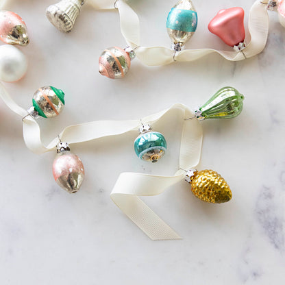 A set of 20 Multicolor Ornaments strung on a cream ribbon, on a marble table.