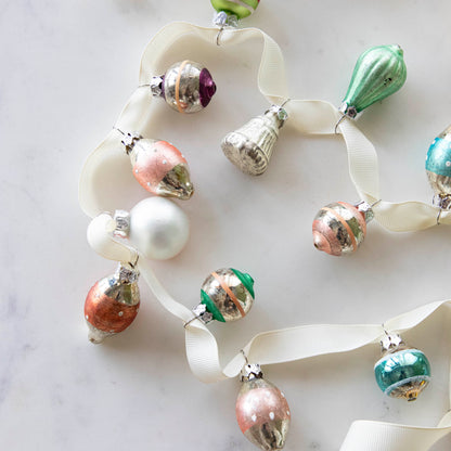 A set of 20 Multicolor Ornaments strung on a cream ribbon, on a marble table.