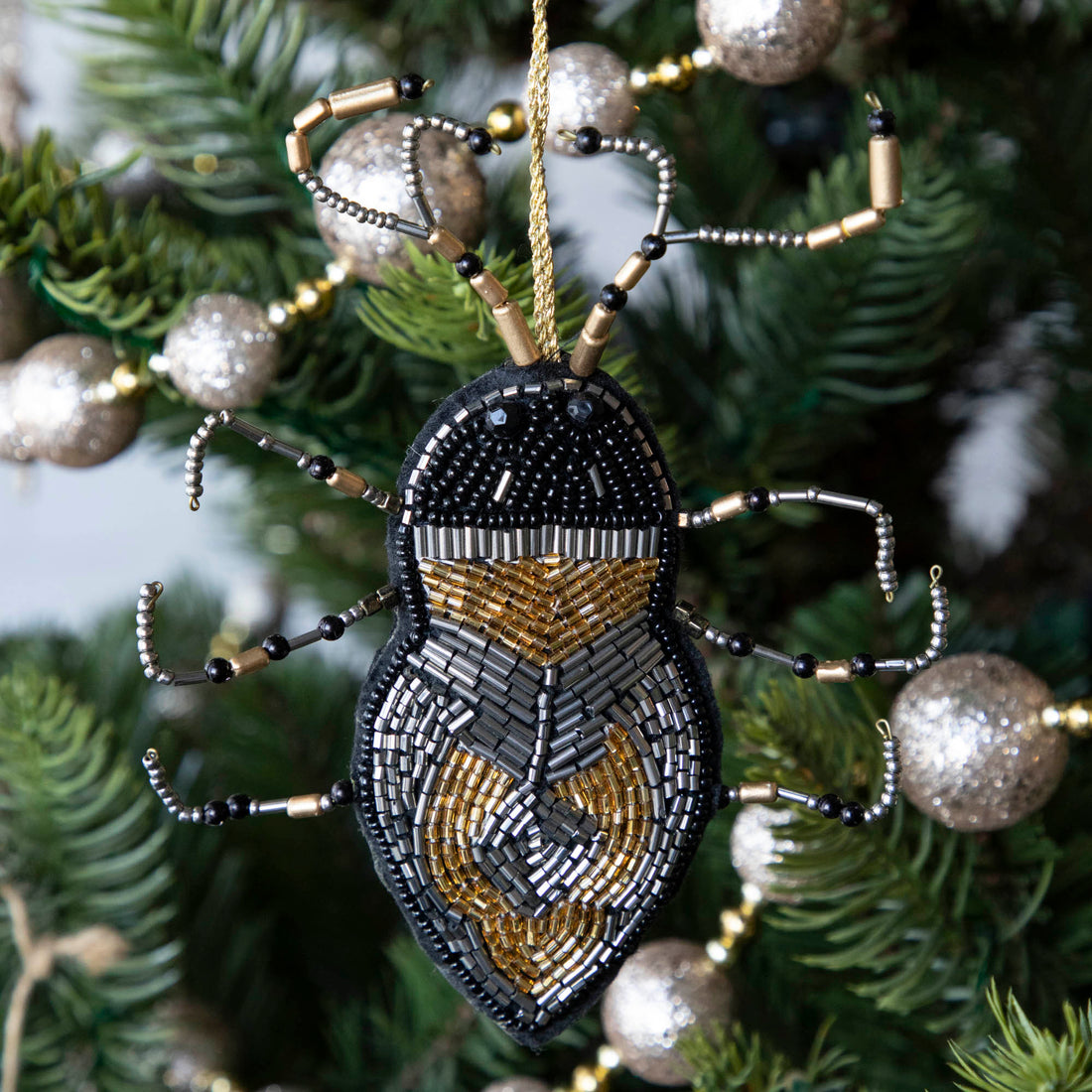 A holiday décor Christmas tree decorated with silver baubles and unique Shi Shi beaded insect ornaments.