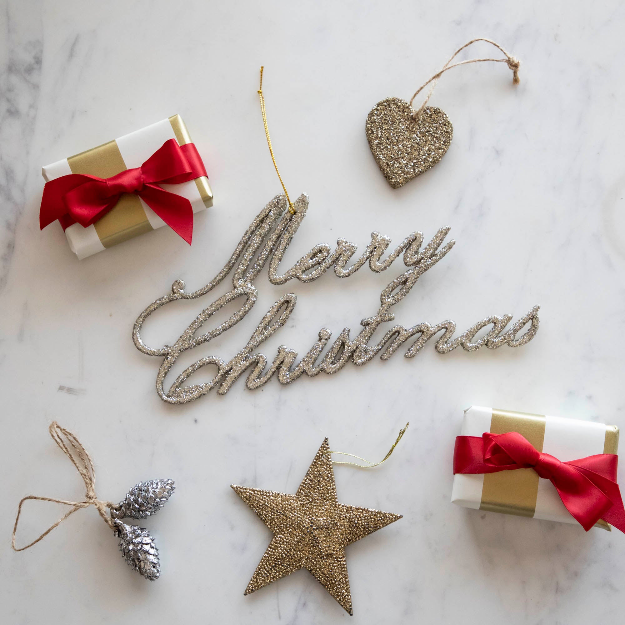 Champagne Merry Christmas ornament on a table with various ornaments and wrapped gifts.