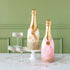 Pink and gold papermache Oversized Champagne Bottles, styled with coupe glasses filled with glitter.