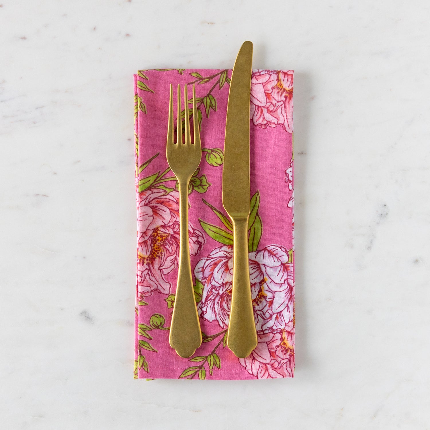Gold fork and knife on a pink floral napkin against a white marble background.