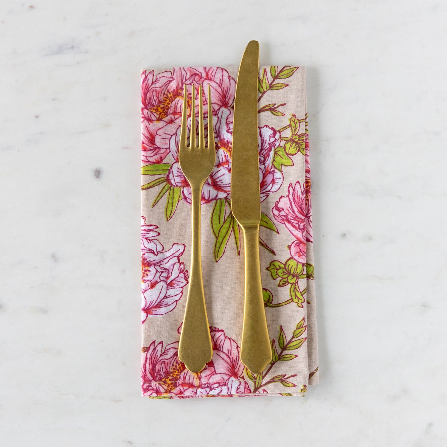 Gold fork and knife on a floral-patterned napkin against a marble background.