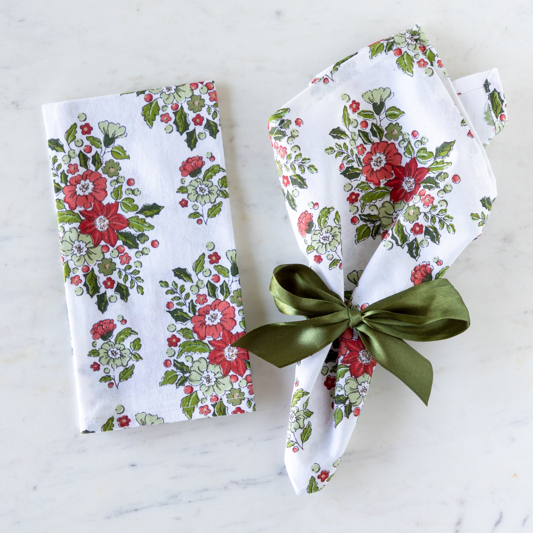 Holly & Berry Ivory Napkins, one tied with Moss Green Fancy Ribbon and the other folded on a marble table.