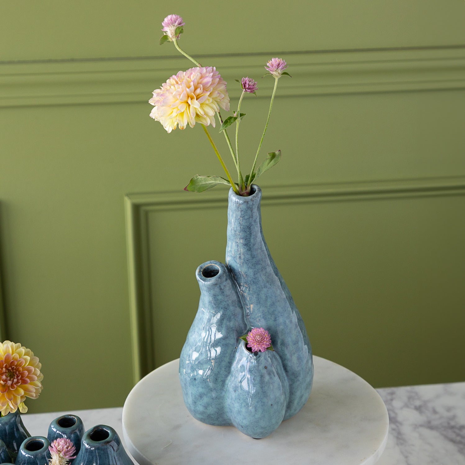 Blue ceramic vase with flowers on a marble surface against a green wall.