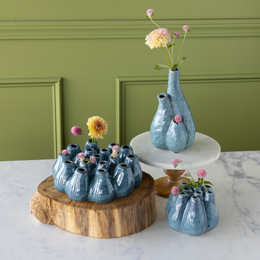 Set of blue ceramic vases with flowers on a marble surface against a green wall.