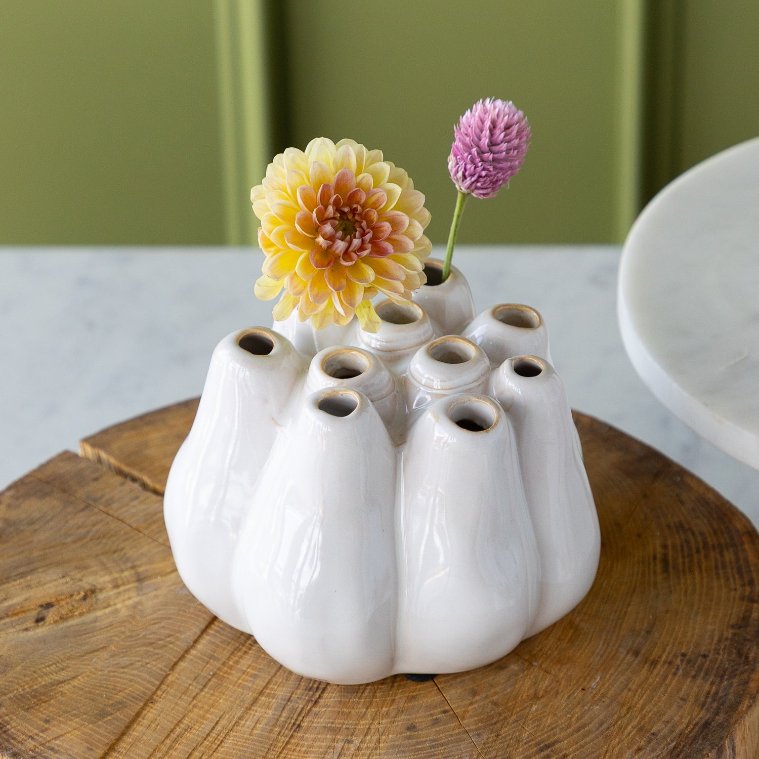 White ceramic vase with multiple holes holding a flower, on a wooden surface.