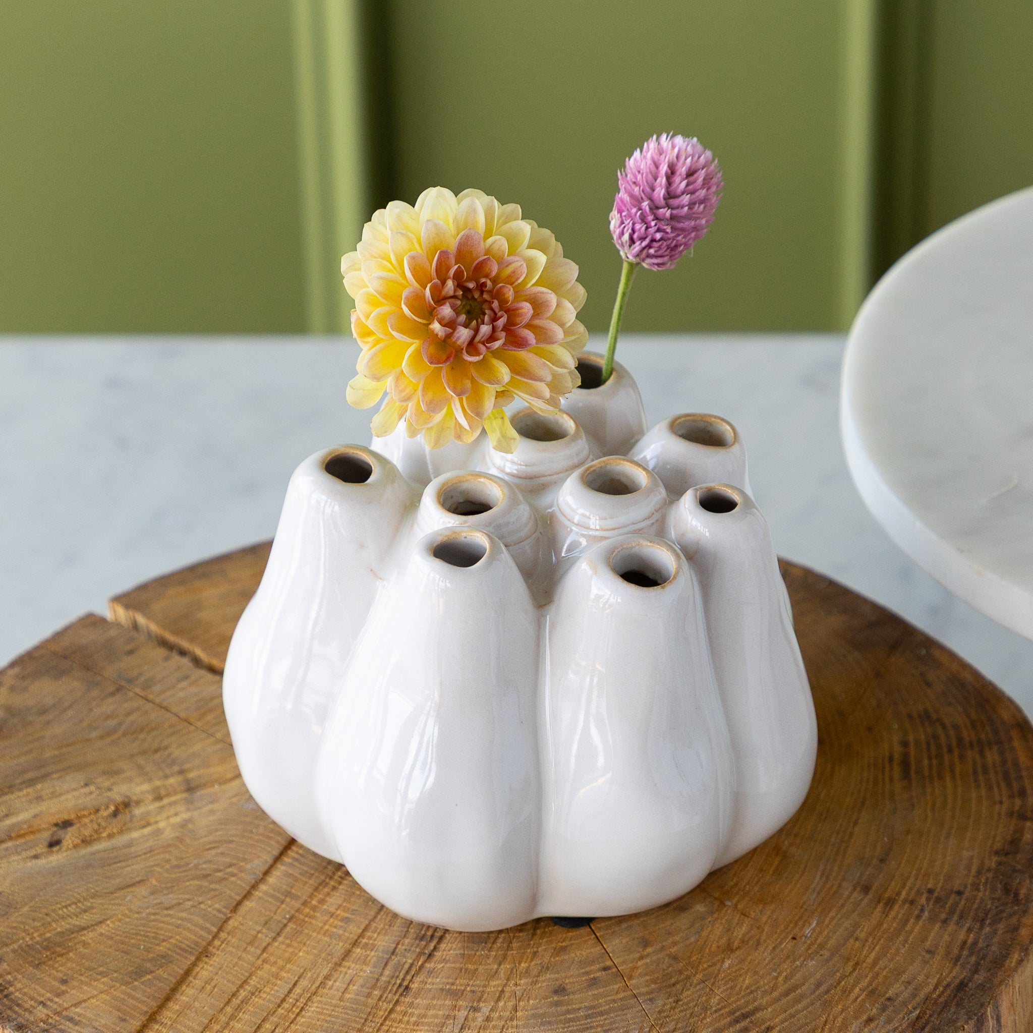 White ceramic vase with multiple holes holding a flower, on a wooden surface.