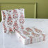 A stack of rectangular paper napkins with a pink and burgundy floral vine pattern on a white background, displayed on a white marble tabletop against an olive green paneled wall.