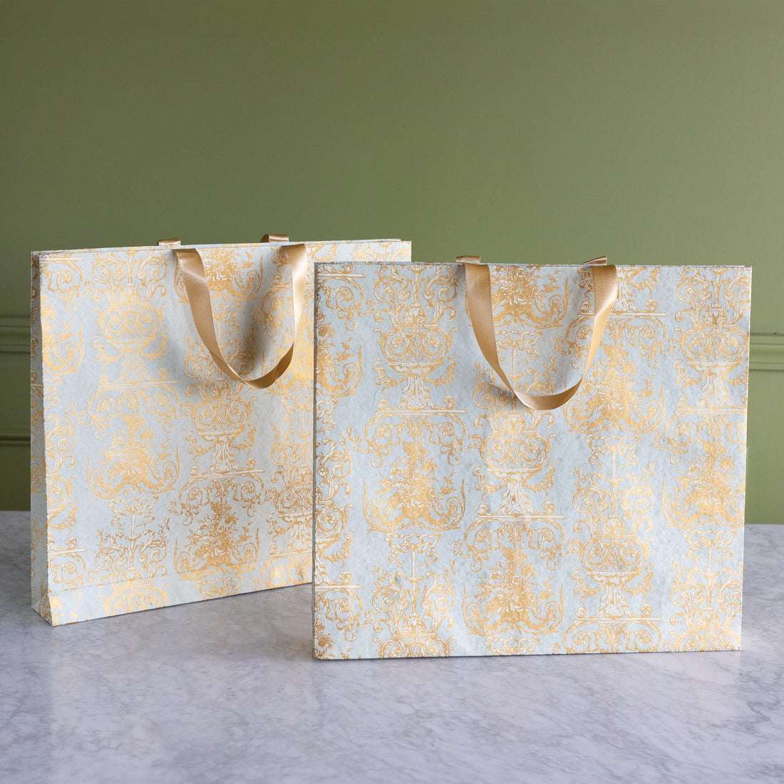 Two decorative paper bags with gold patterns on a gray surface and green background.