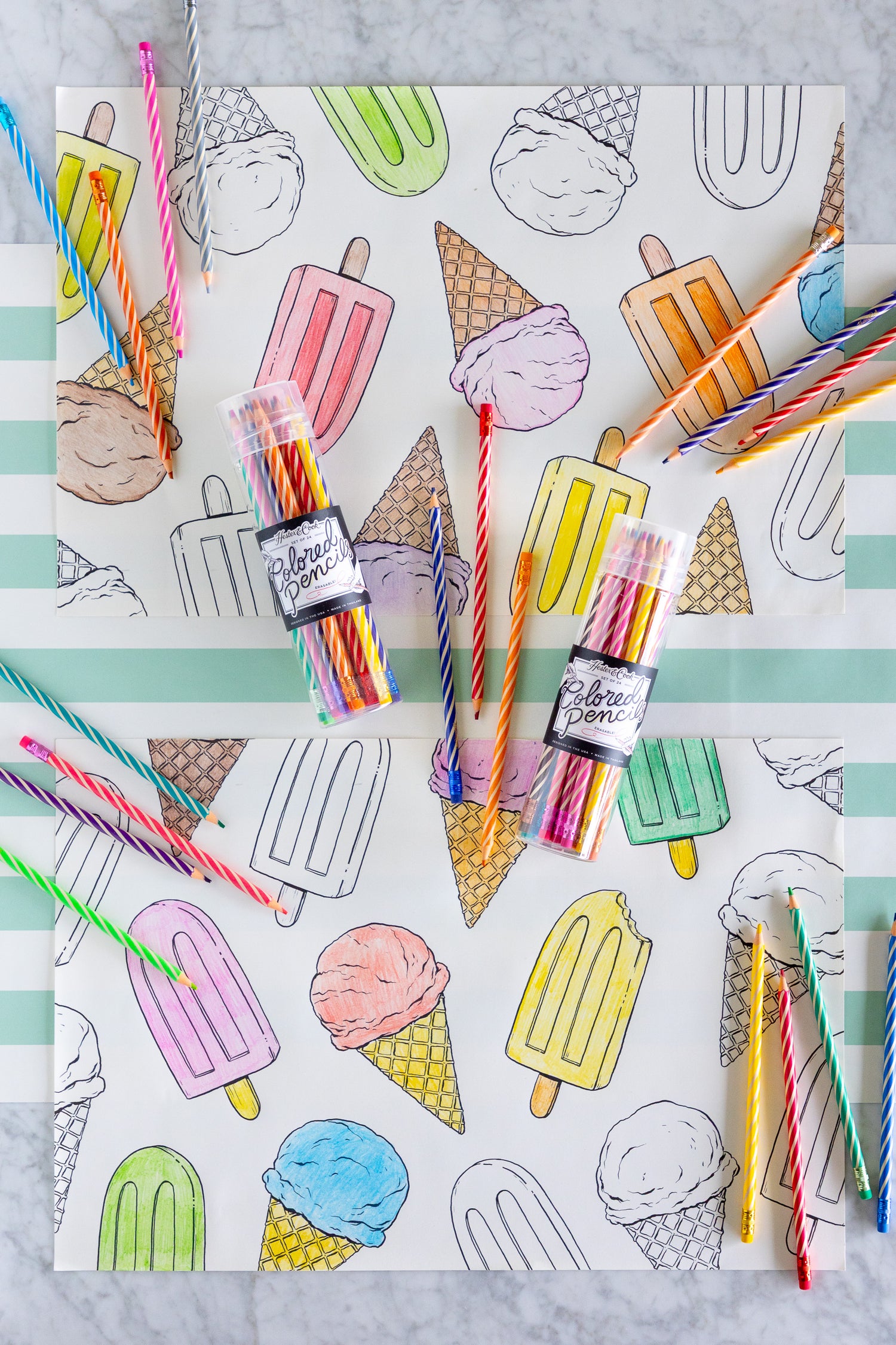 Coloring placemats with ice cream and popsicle illustrations and colored pencils on a striped table runner.