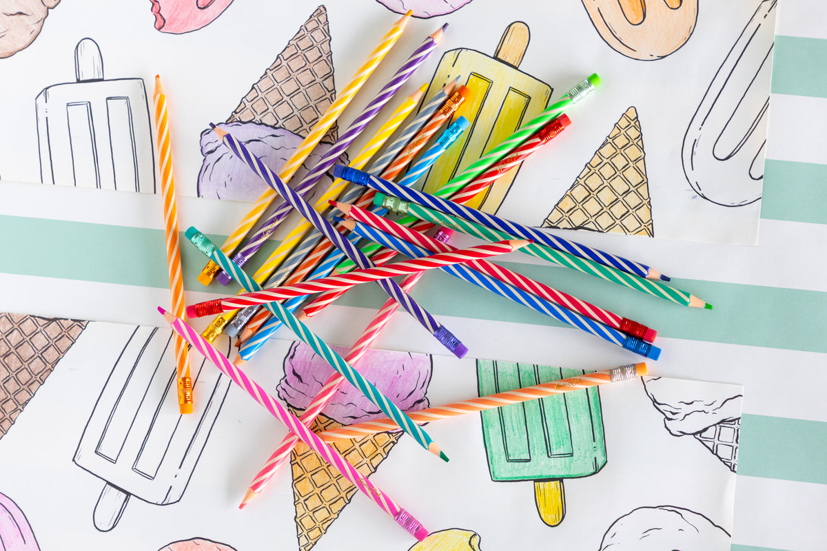 Coloring placemats with ice cream and popsicle illustrations and colored pencils on a striped table runner.