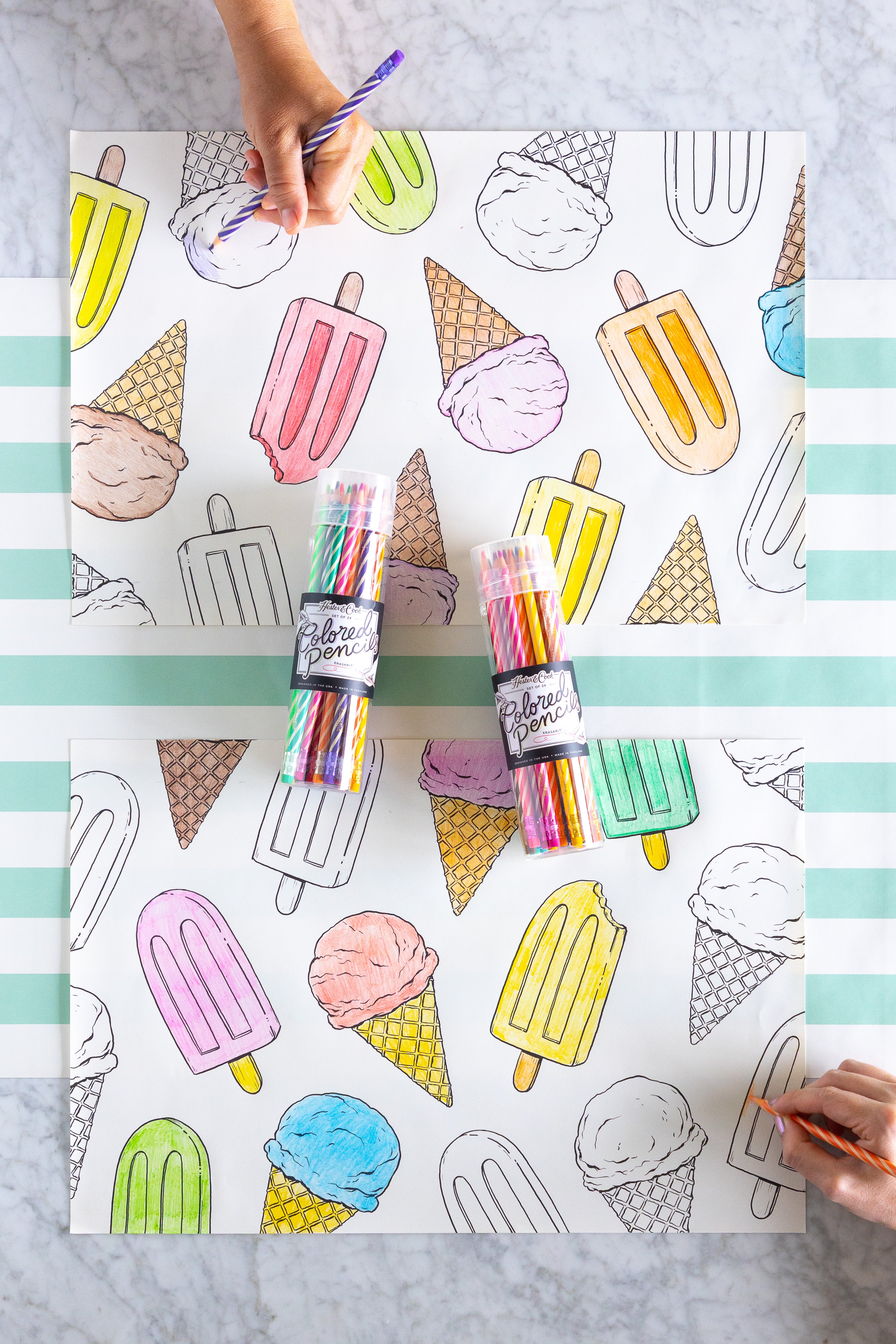 Coloring placemats with ice cream and popsicle illustrations and colored pencils on a striped table runner.
