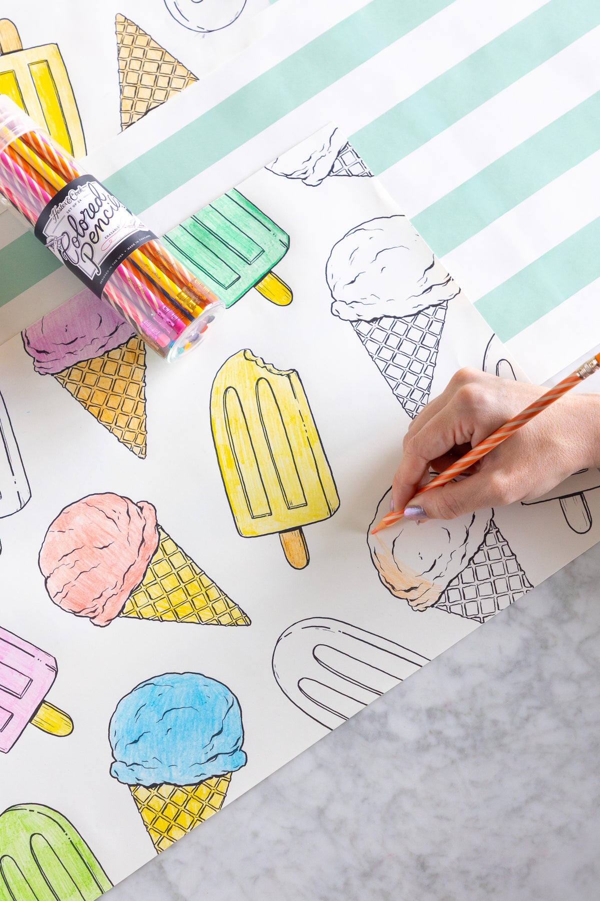 Coloring placemats with ice cream and popsicle illustrations and colored pencils on a striped table runner.