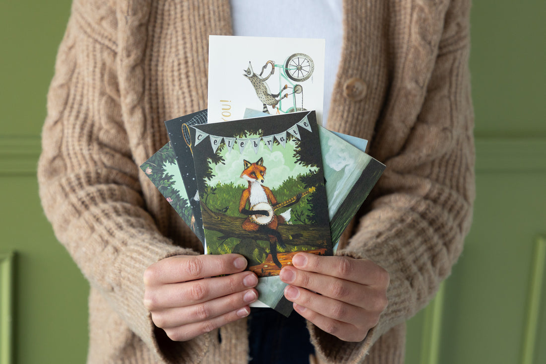 Person holding a collection of nature-themed greeting cards against a green background.