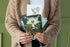 Person holding a collection of nature-themed greeting cards against a green background.