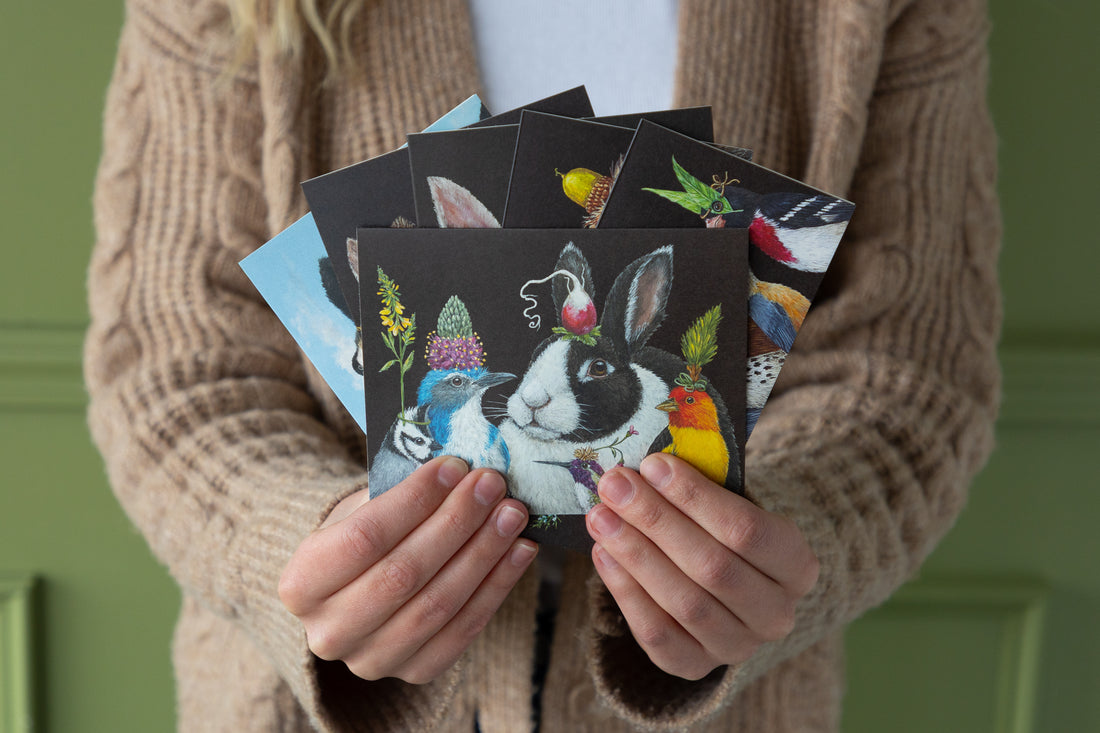 Person holding a collection of postcards with animal illustrations against a green background.
