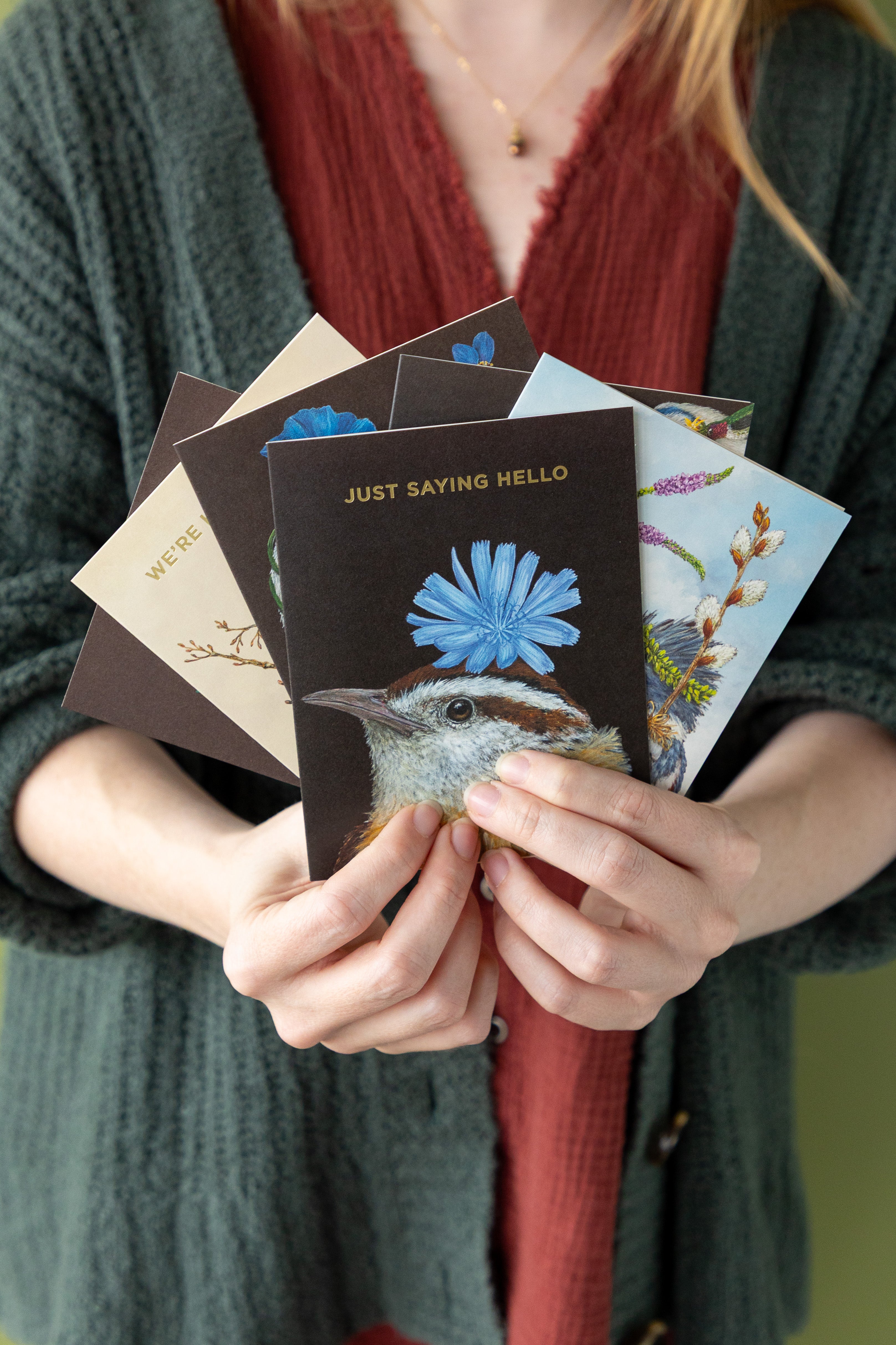 Person holding a stack of greeting cards with various designs and text.