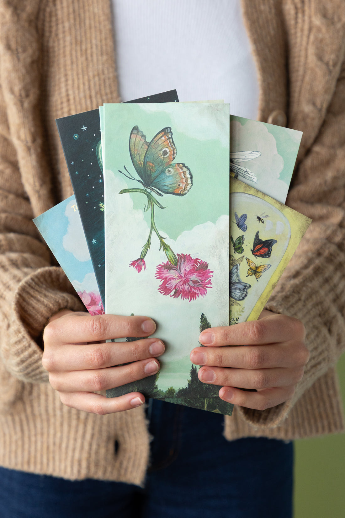 Person holding a fan of greeting cards with nature-themed designs.