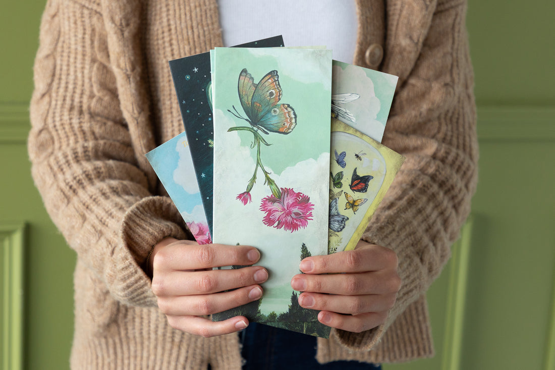 Person holding a collection of colorful greeting cards with butterfly and floral designs against a green background.