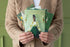 Person holding a set of greeting cards with artistic designs on a green background.