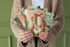 Person holding a collection of colorful greeting cards against a green background.