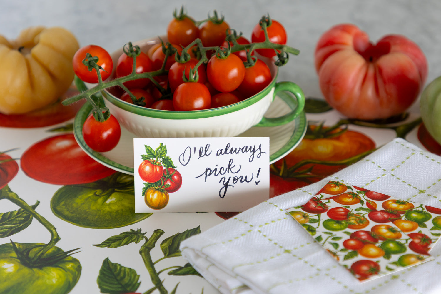 A tiny note with tomatoes on it in front of a bowl filled with cherry tomatoes.  