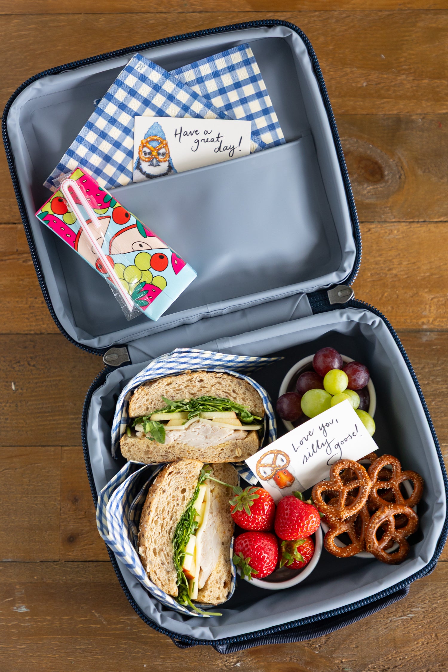 A lunchbox filled with food items and 2 tiny notes with messages on them tucked inside. 