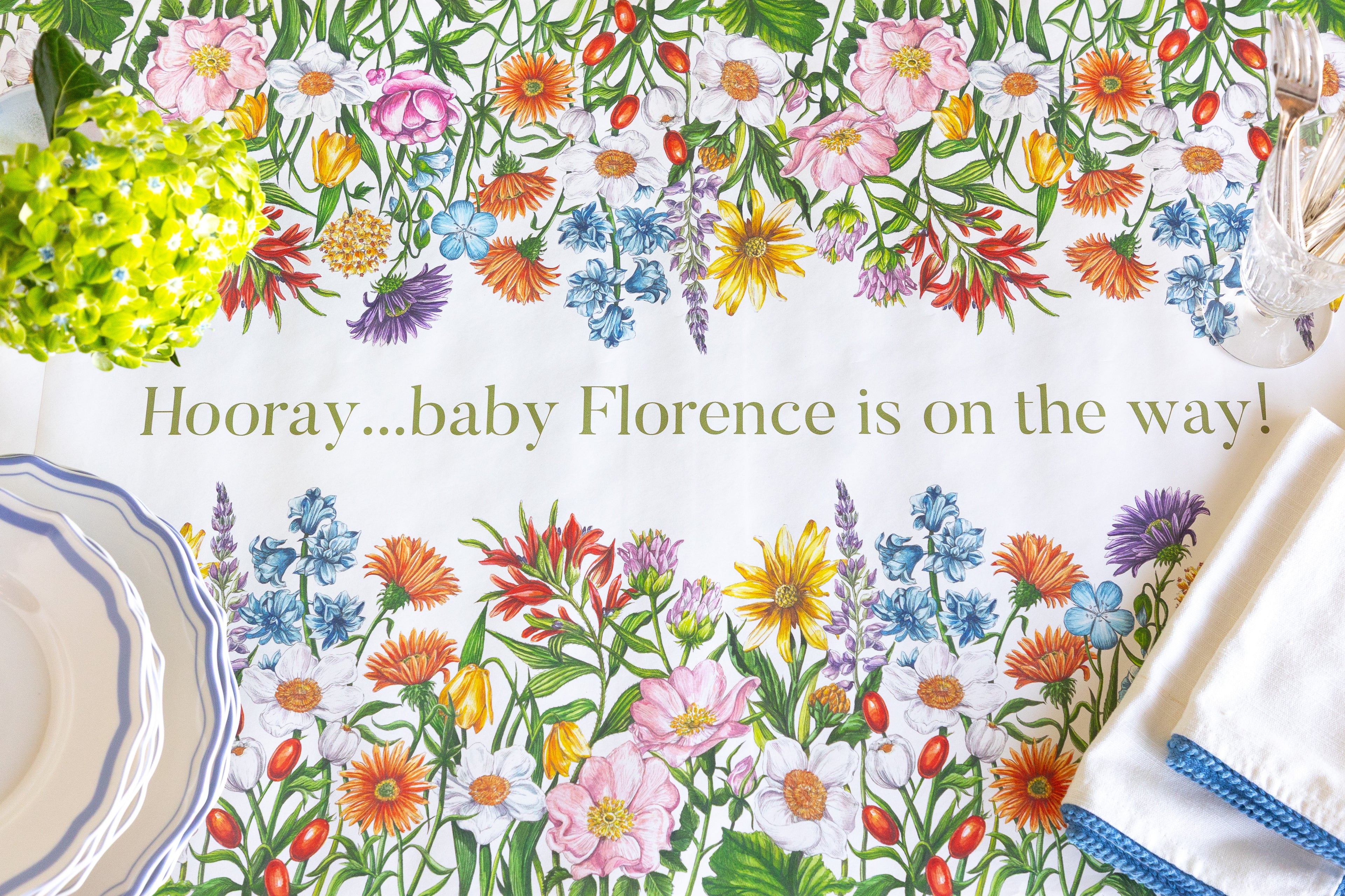 A white paper table runner  with a colorful wildflower border and the text &