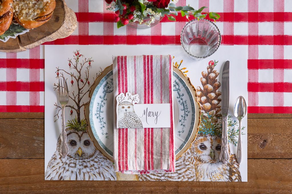 Christmas-themed table setting with owl design placemat, red and white striped napkin, and festive decorations.