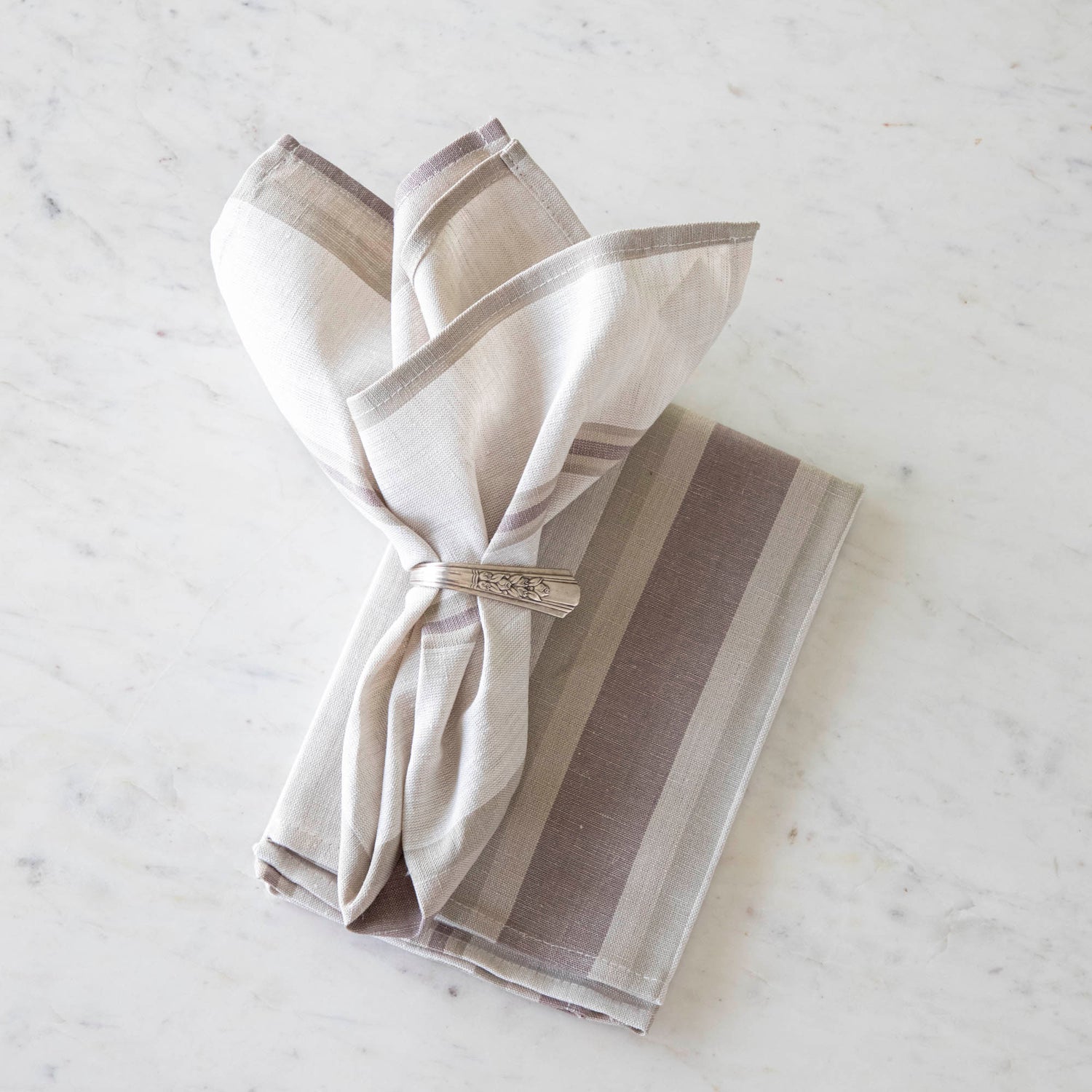 Dusty Pastel Striped Cloth Napkin in a vintage silver napkin ring on top of the same napkin, on a marble table.