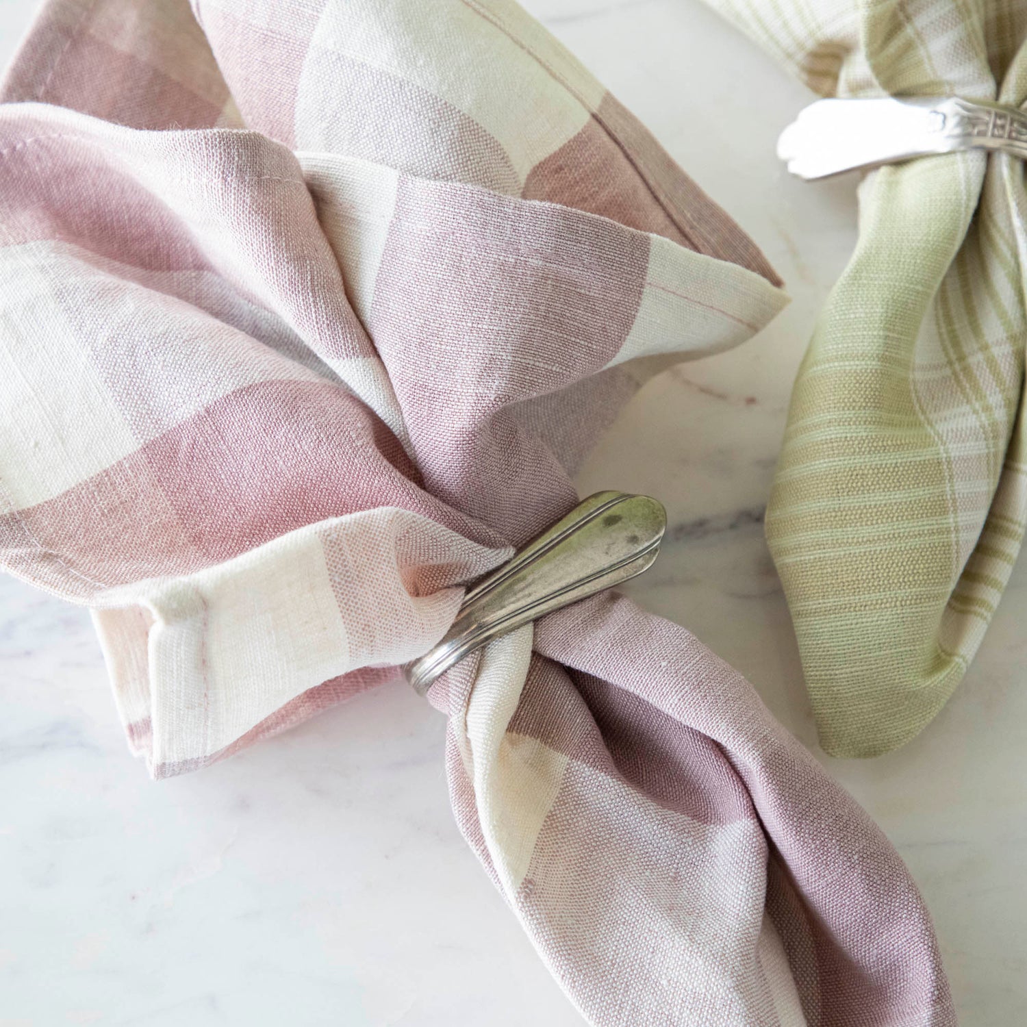 Close up of the Vintage Rose Buffalo Check Cloth Napkin in a silver napkin ring, next to the Grapefruit Plaid napkin.