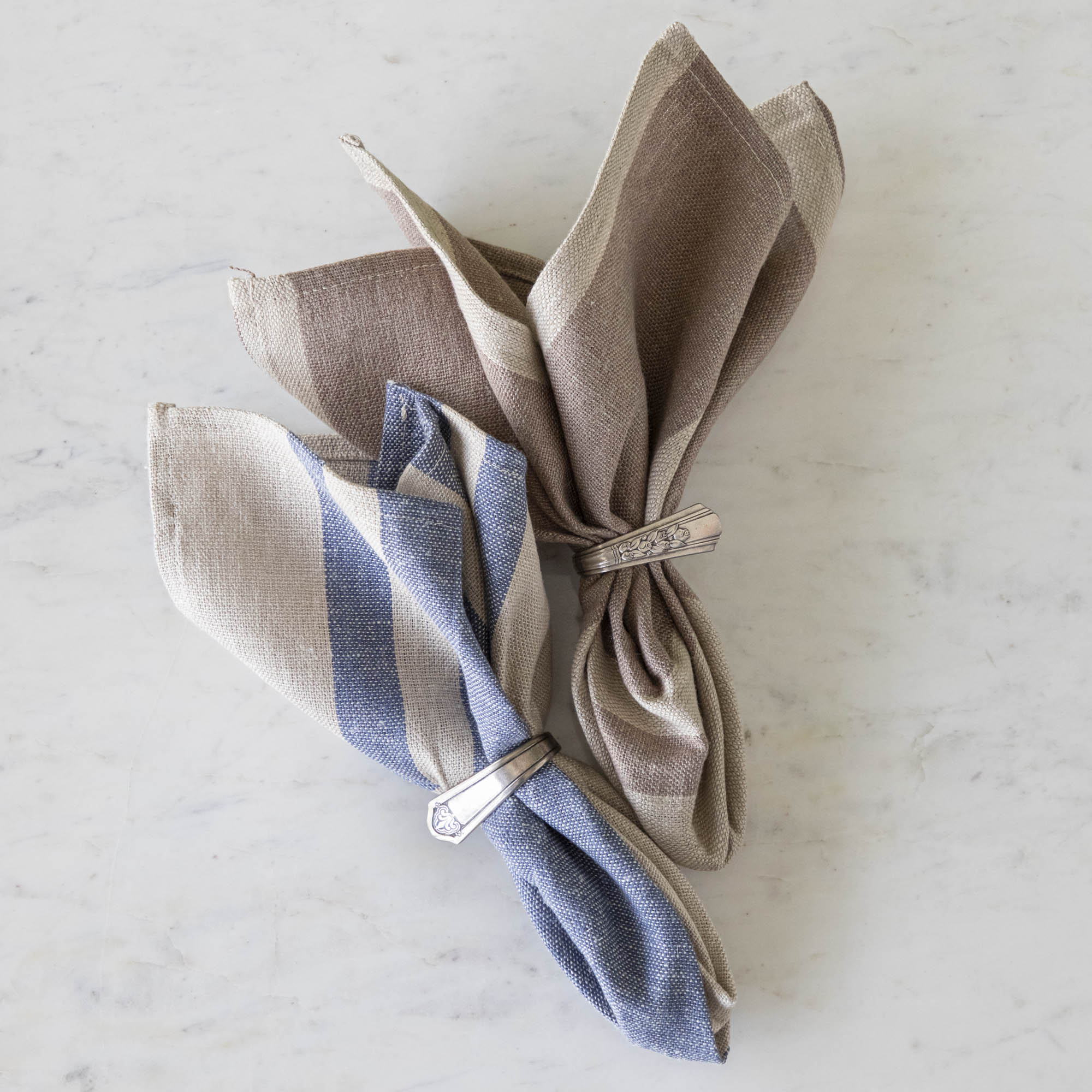 Dusty Rose Striped Woven Linen Napkin and Vintage Blue Striped Woven Linen napkin in vintage silver napkin rings on a marble table.