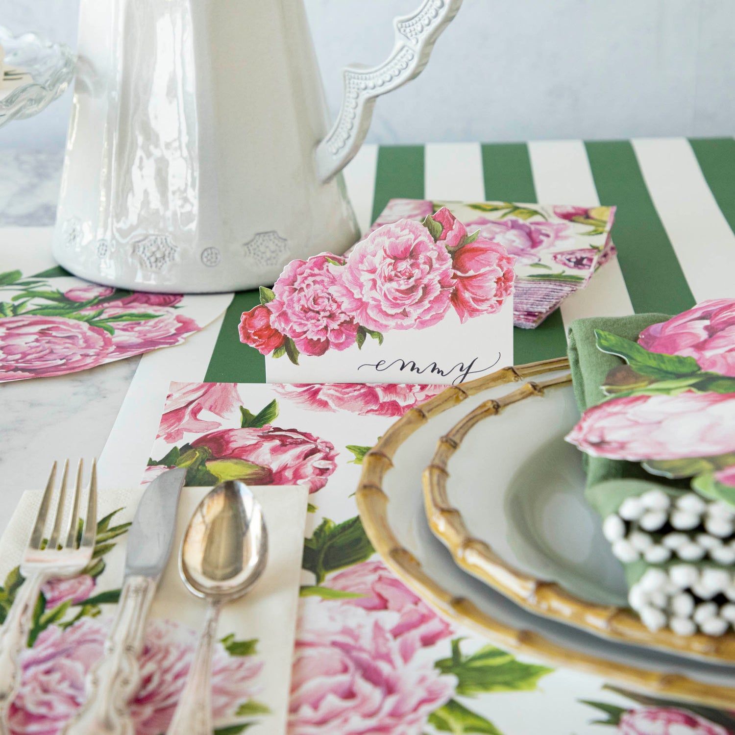 An elegant place setting featuring a Peony Place Card labeled &quot;Emmy&quot; standing behind the plate.