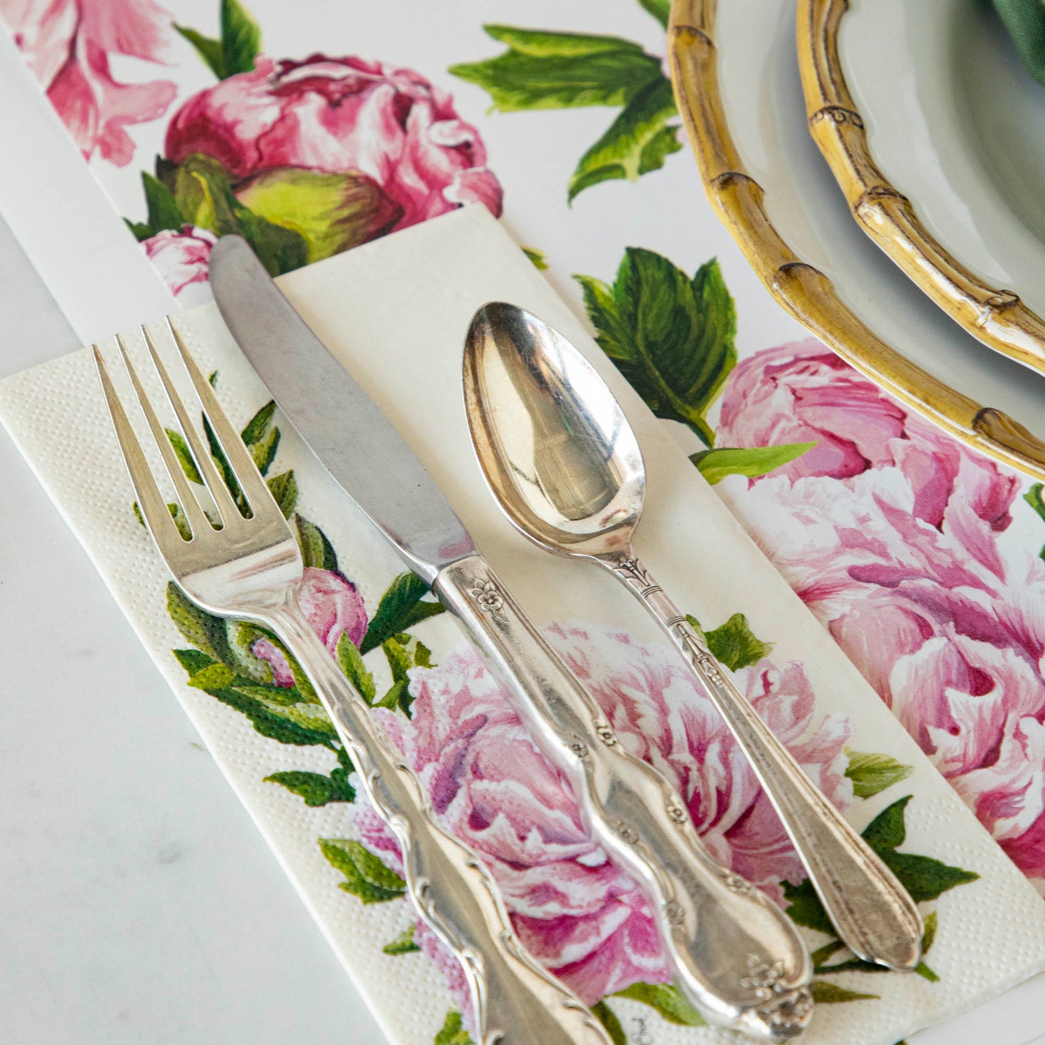 A party table setting with fresh Peony Napkins by Hester &amp; Cook and silverware.