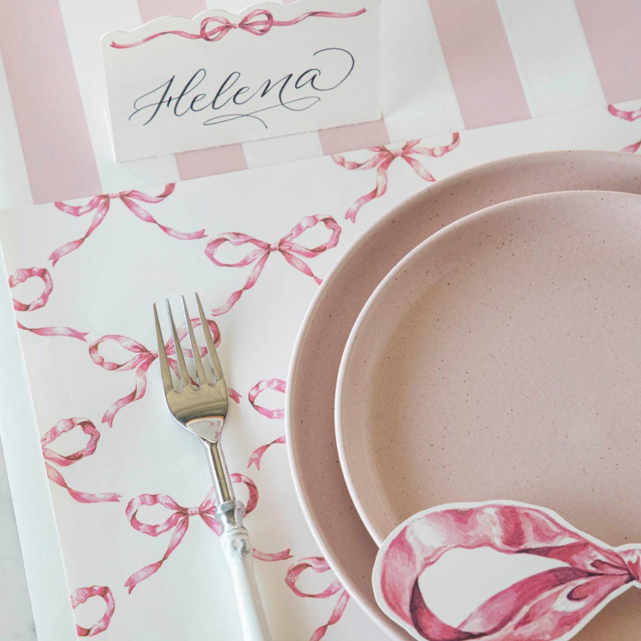 A Pink Bow Lattice Placemat with a plate and fork on a table made by Hester &amp; Cook.