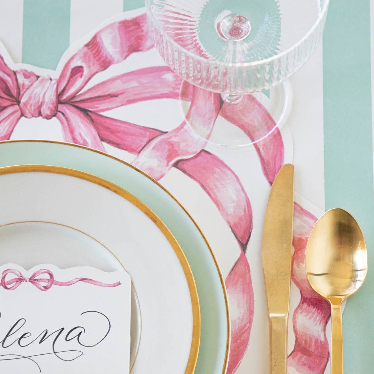 A whimsy place setting with a gold spoon and fork on a Hester &amp; Cook Die-cut Pink Bow Placemat.