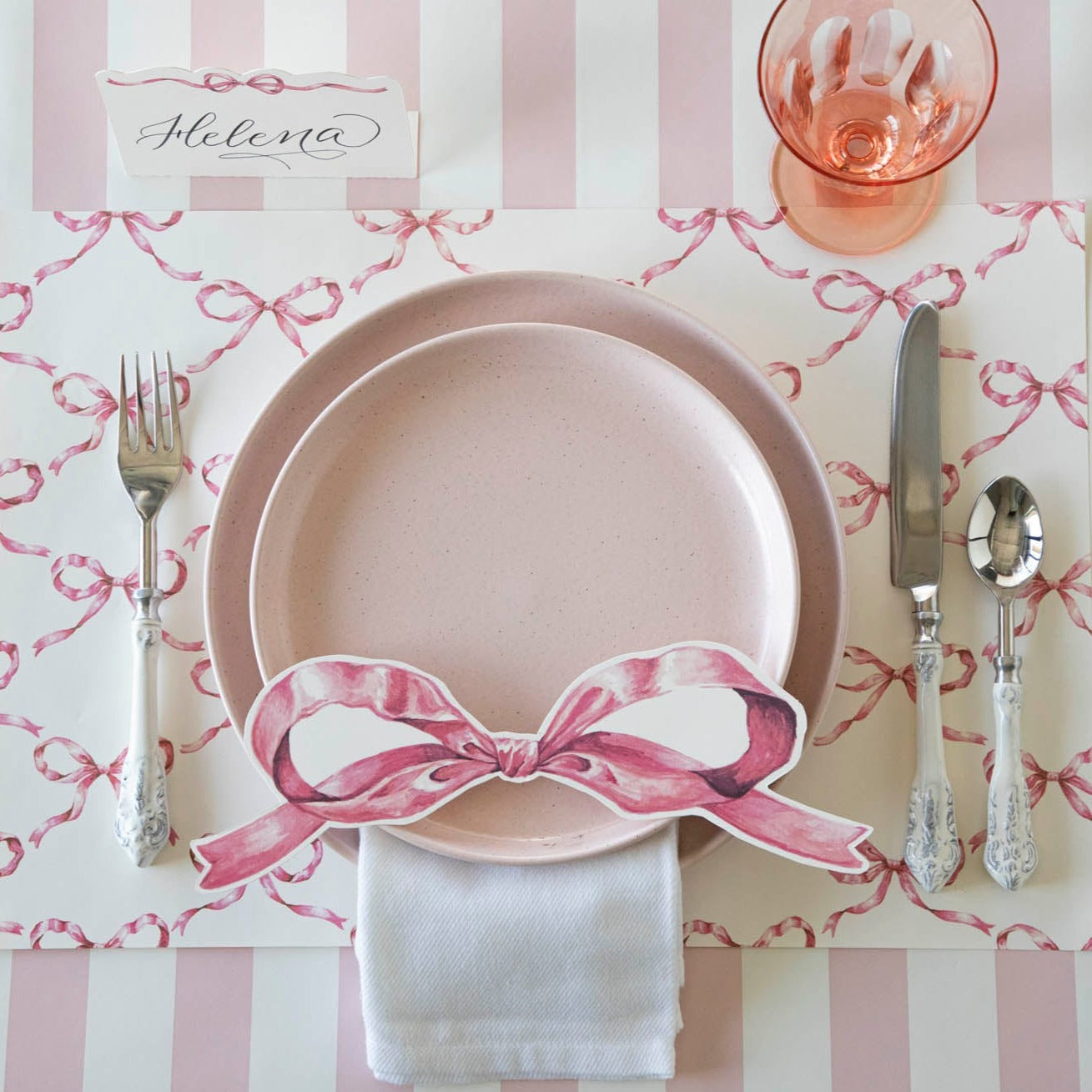 A Pink Bow Lattice Placemat by Hester &amp; Cook with silverware on a table.