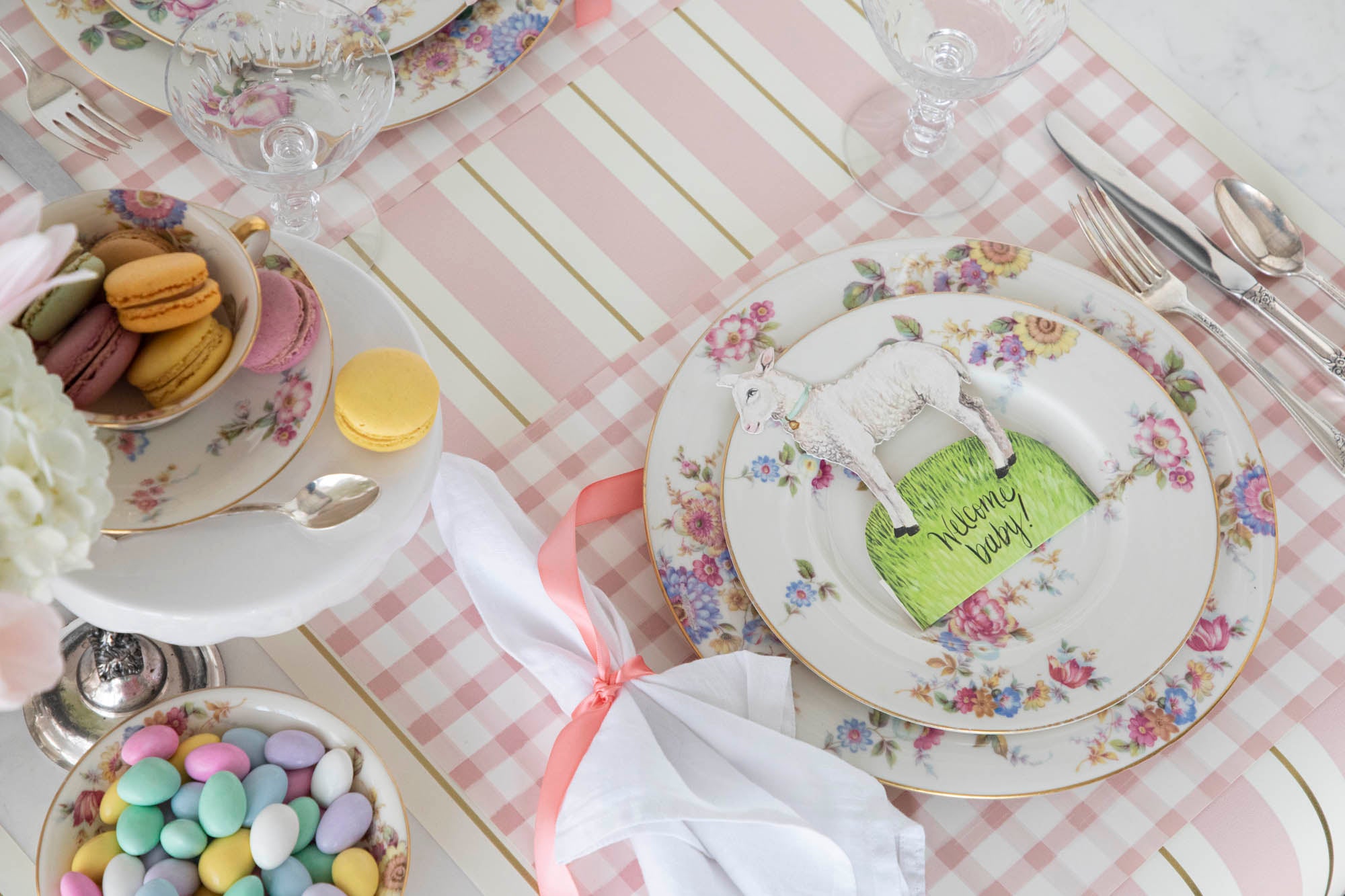 An Easter table setting with pink and white plates, napkins, and adorable Hester &amp; Cook Little Lamb Place Card featuring an Easter Garden Story.