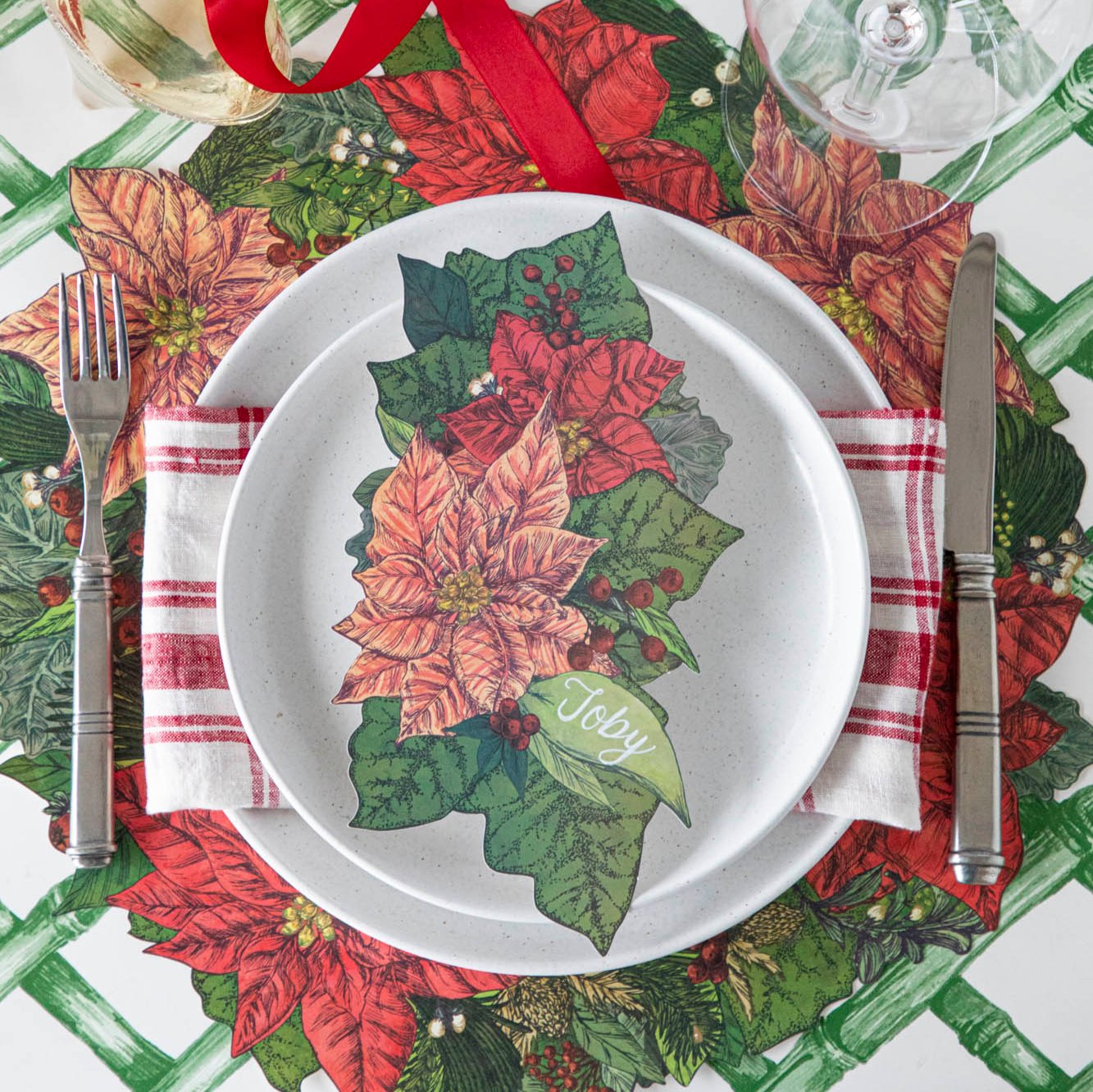 An elegant table setting with the Poinsettia Table Accent with &quot;Toby&quot; written on the leaf, resting on salt dinner plates, the Die-cut Poinsettia Wreath Placemat and Green Lattice Runner underneath.