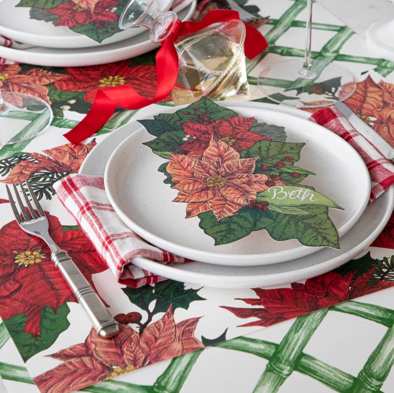 An elegant table setting with the Poinsettia Table Accent with &quot;Beth&quot; written on the leaf, resting on salt dinner plates, the Poinsettia Placemat and Green Lattice Runner underneath.