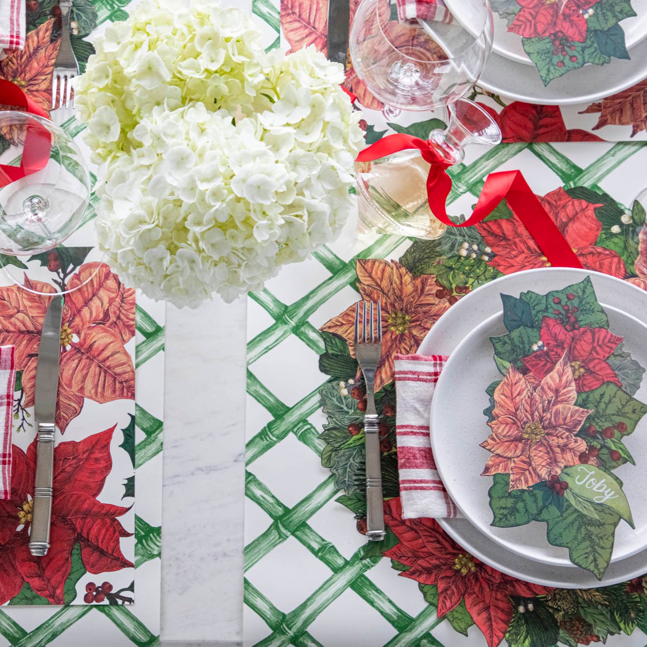 An elegant table setting with flowers, and the Die-cut Poinsettia Placemat on the Green Lattice Runner,  featuring the Poinsettia Table Accent with &quot;Toby&quot; written on it, resting on a plate.