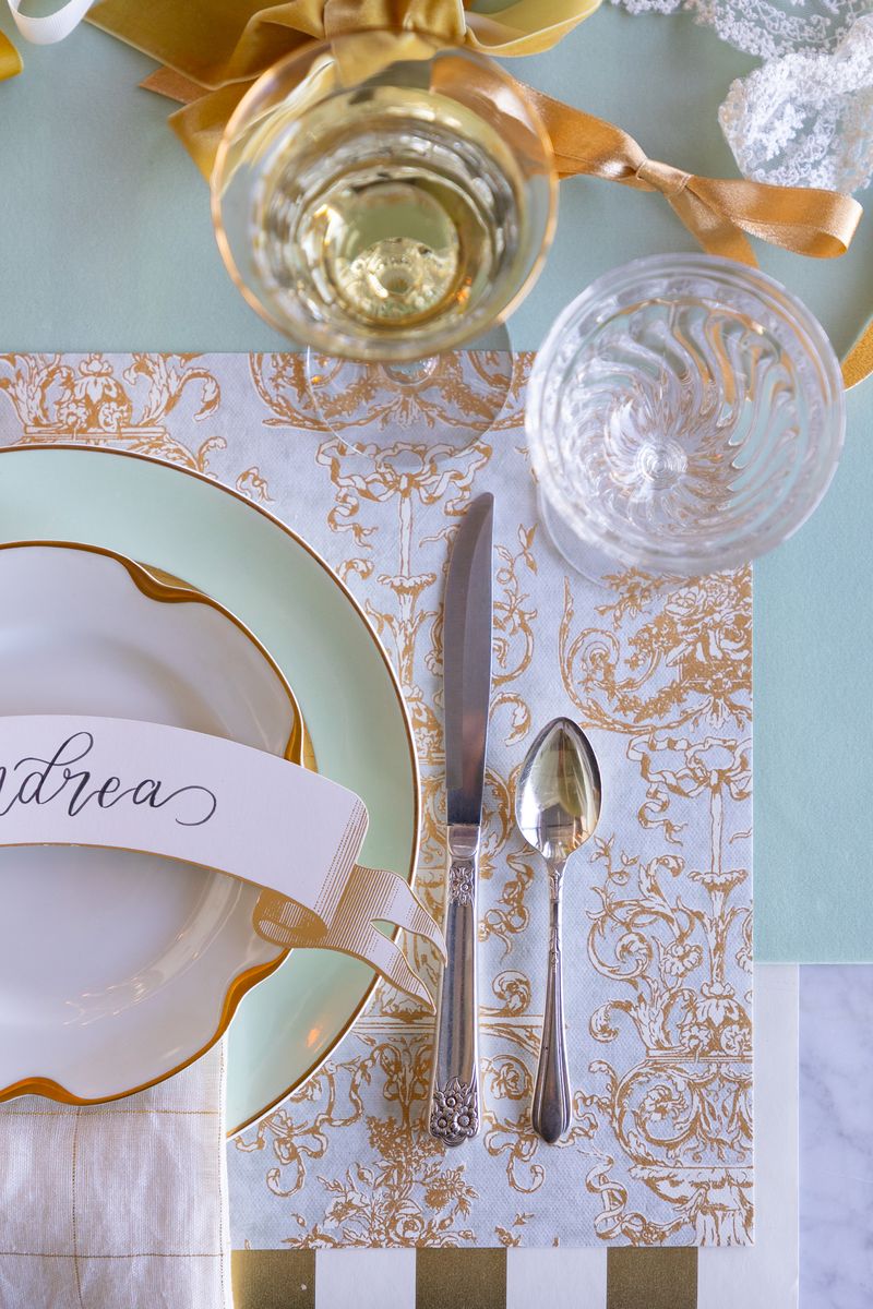Decorative table setting with gold accents on a light blue and white patterned tablecloth.