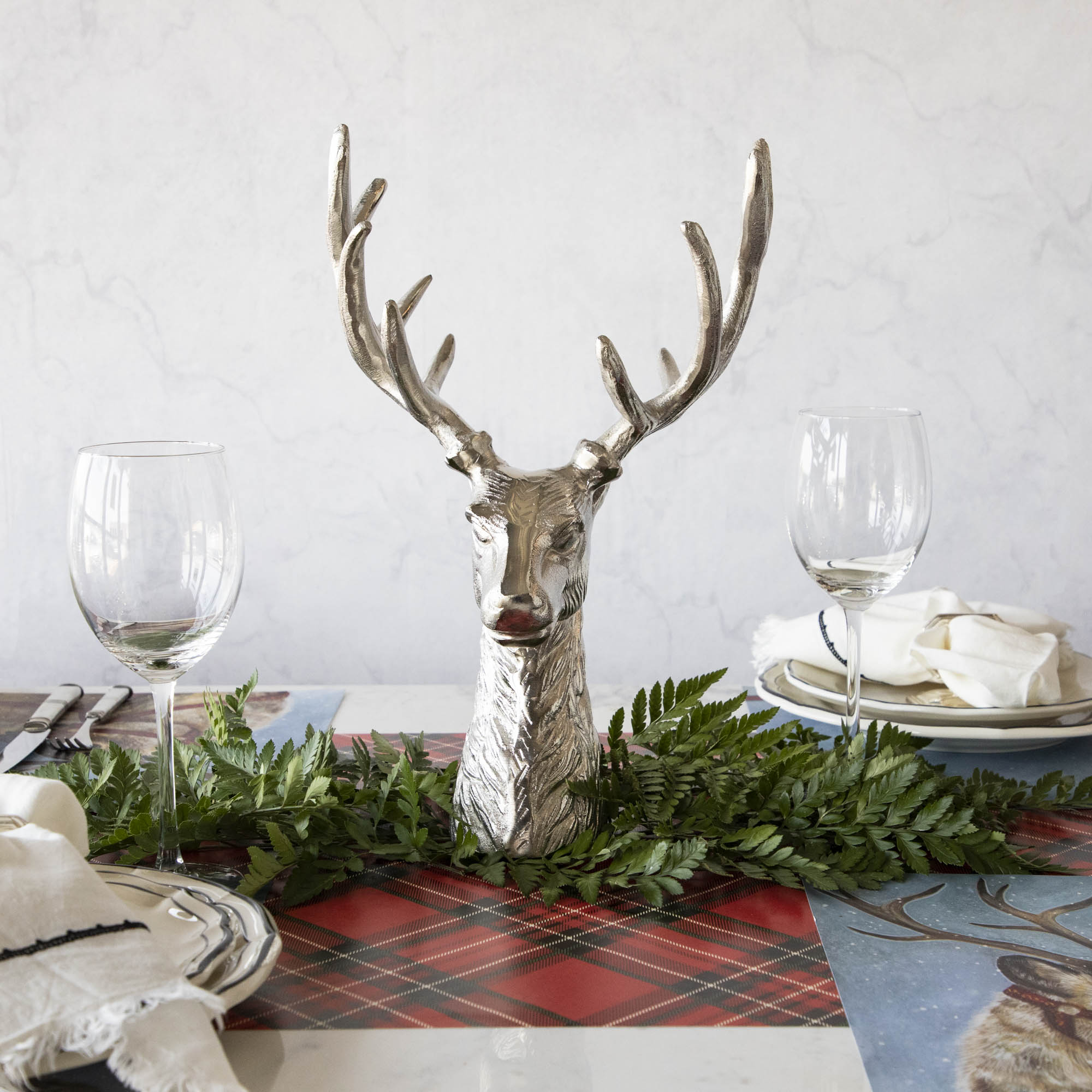 An aluminum Reindeer Bust, in the center of a woodland themed table setting, surrounded by a leaf garland.